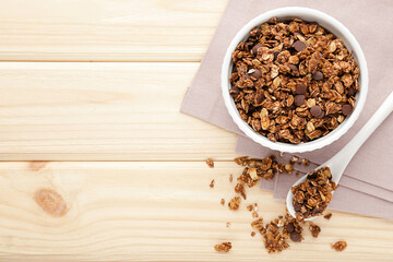 Tasty chocolate granola in bowl, spoon and napkin on brown wooden background