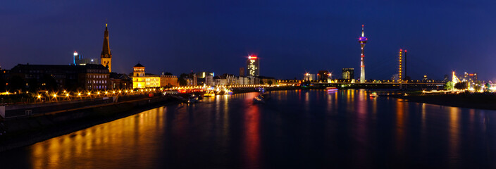 Night phanorama of Dusseldorf city from a bridge across Rhine. Beautiful city lights are reflecting into the calm waters of the river.