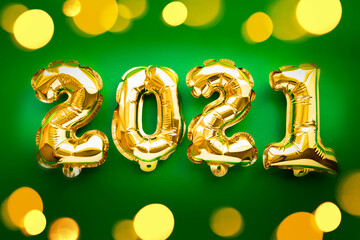 Happy New year 2021 celebration. Gold foil balloons numeral 2021 and festive bokeh lights on green background. Flat lay.