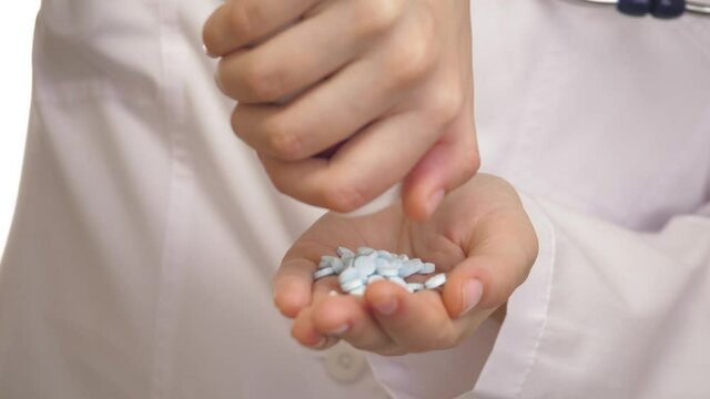 Close-up of caucasian doctor's hand who is counting blue pills by his finger. Young man is picking over the tablets on his palm. There is a theme of drug treatment. Concept of medicine and healthcare