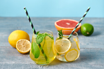 Fresh homemade lemonade with lime, mint, rosemary, thyme and ice in the glass with paper straw on blue background