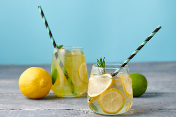 Fresh homemade lemonade with lime, mint, rosemary, thyme and ice in the glass with paper straw on blue background