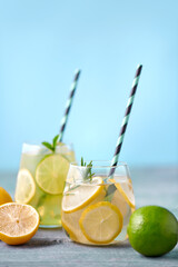 Fresh homemade lemonade with lime, mint, rosemary, thyme and ice in the glass with paper straw on blue background