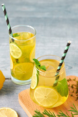 Fresh homemade lemonade with lime, mint, rosemary, thyme and ice in the glass with paper straw on blue background