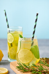 Fresh homemade lemonade with lime, mint, rosemary, thyme and ice in the glass with paper straw on blue background