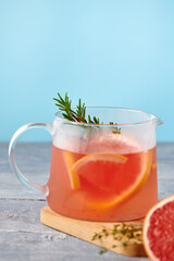Fresh homemade lemonade with grapefruit and rosemary in the glass carafe on blue background