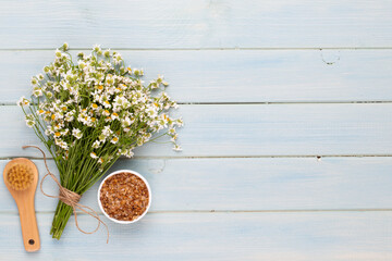 Sea salt, aromatherapy oil in bottles and chamomile on vintage wooden background.