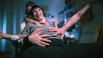 A pregnant woman is sitting in a chair. The hands of family members touch the stomach, stroke it. Expectation of a child in a large family.
