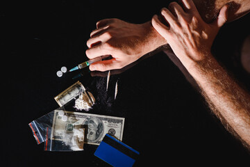 Man's hands trying to abstain from drugs on dark table with cooked heroine, pills, spoon and plastic bag. Concept for drug addiction and International Day against Drug Abuse, top view