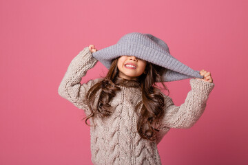 little brunette girl with long hair in winter clothes on a pink background in the Studio. knitwear for children, space for text