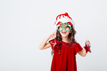 funny little girl in a Santa hat and glasses holding Christmas toys on a white background of isolate. the concept of Christmas, the space for text