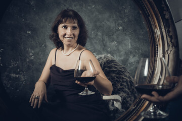 Obraz na płótnie Canvas Cheerful 40 years old woman in classic dress with glass of wine