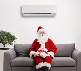 Santa claus sitting on a sofa with a present under an air conditioner