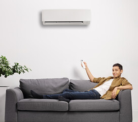 Young man sitting on a sofa and putting an air conditioning unit on with a remote control