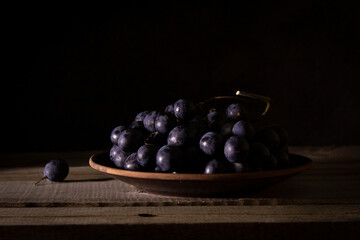 Ripe bunch of red grapes on a clay plate on a wooden table, shot in low key
