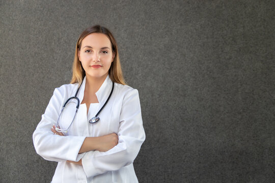Crossing her arms confidently, female doctor posing in studio with stethoscope around her neck, standing straight and looking into camera. Copy space. Healthcare, medicine and profession concept.