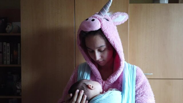 Mother And Baby In Sling And Unicorn Onesie Staying At Home