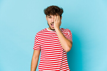 Young arab man on blue background having fun covering half of face with palm.