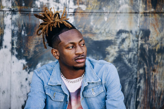Handsome African-American Young man wearing a denim jacket with dreadlocks and facial hair and looking away off to the side