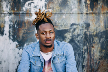 Handsome African-American Young man wearing a denim jacket with dreadlocks and facial hair and looking at the camera very serious