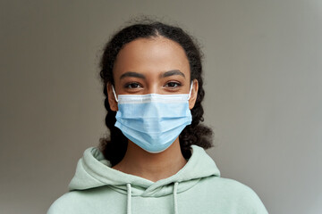 African american teen girl wearing face mask looking at camera isolated on grey background. Mixed race teenager during coronavirus. Children safety for covid protection, close up headshot portrait. - Powered by Adobe