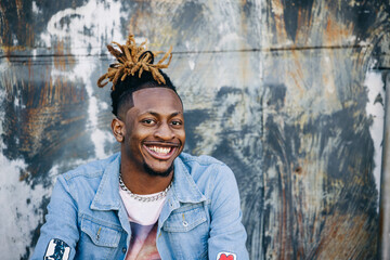 Handsome African-American Young man wearing a denim jacket with dreadlocks and facial hair and looking at the camera and smiling - Powered by Adobe