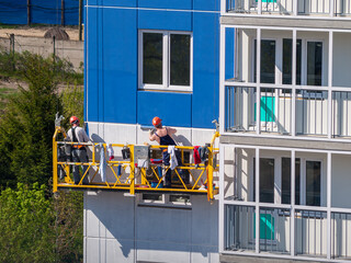 construction workers installers high-rise workers industrial climbers, painters on the lift paint...