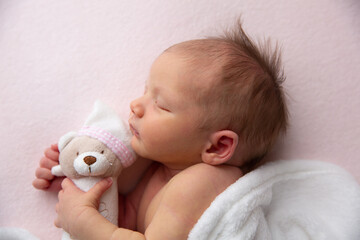 A cute little newborn baby is sleeping with a stuffed toy on a blanket.