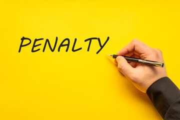 Male hand writes in black pen the word penalty on a yellow background with copy space. Business concept photo