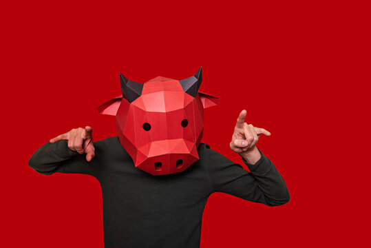 Young man in red 3d mask of a bull cow on the head on an isolated background. Person shows with gestures that he gores. Blank for banner, template, place for advertising text. Businessman. Copy space