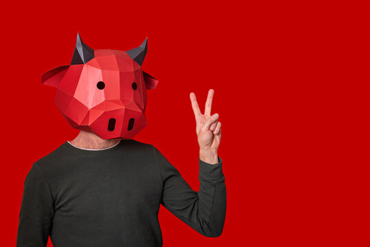 Young man in red 3d mask of bull cow on the head on an isolated background. He is showing the peace sign with gestures. Blank for banner, template, place for advertising text. Businessman. Copy space