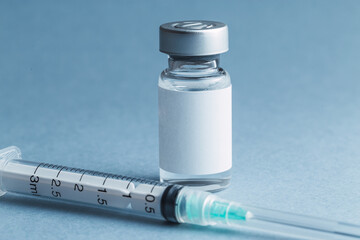 A glass vial of a medical drug vaccine next to a sterile hypodermic syringe