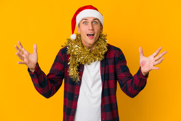 Young caucasian man with christmas hat holding a present isolated on yellow background