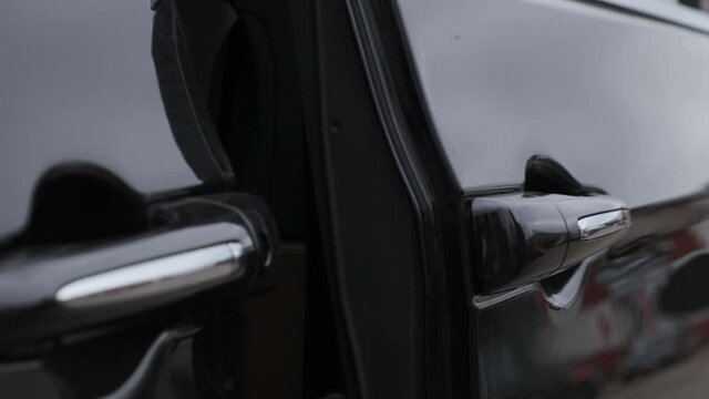 man in black jacket opens door of black minivan with his hand, press button and door slides to the side.