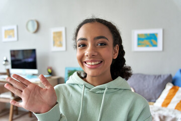 Happy african gen z teen girl waving hand talking to camera in bedroom. Mixed race teenager recording vlog, streaming for social media, video calling in online chat at home. Web cam view headshot - obrazy, fototapety, plakaty