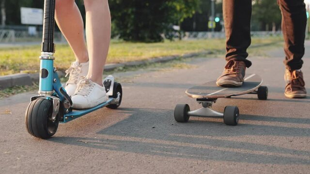 Teens ride skateboard or longboard and scooter together. Close-up of foot, shoes, sneakers. Skating on asphalt track in the city. Skateboarding at summer. Concept of youth, active lifestyle.