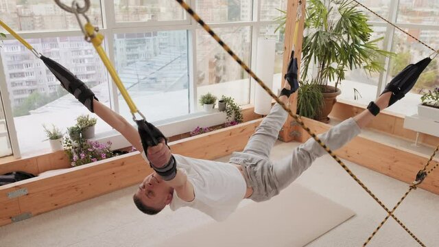Full shot of man attached by ropes to fasteners in lying position making twitching movements on stretching slavonic simulator