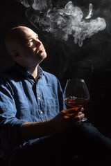 Solid bald man in shirt with glass of whisky and fume studio portrait.