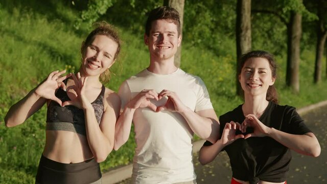 Young people making a heart shape from hands. Portrait of happy friends promote healthy lifestyles. Youngsters in sportwear after jogging smiling to camera. Concept of sports and frienship.