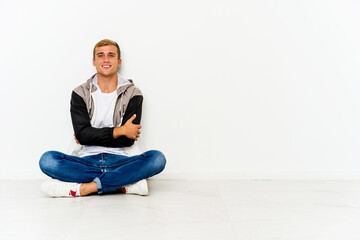 Young caucasian man sitting on the floor who feels confident, crossing arms with determination.