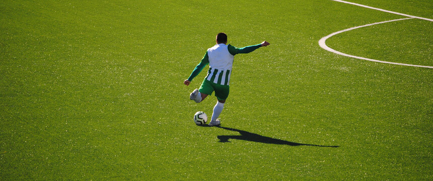 Futebol - jogador com equipamento verde e branco a chutar a bola na zona do meio campo fora da grande área - relvado artificial
