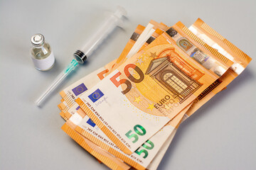 A stack of money and vaccine, medicine and syringe on a gray background