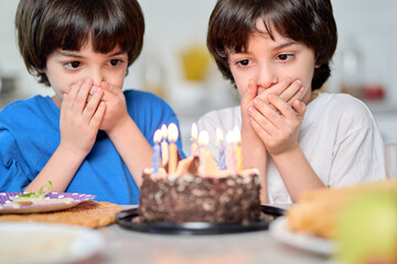 Magic moment. Adorable little hispanic boys looking at birthday cake, making wishes while getting ready for blowing candles