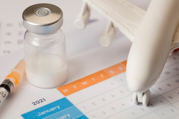 Glass vaccine vial, with syringe, and plane, in calendar 2021