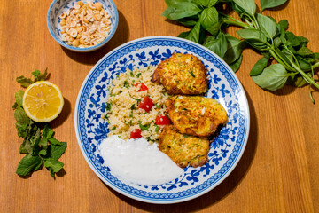 Healthy plate with fried vegetables meatballs and yogurt sauce. Mediterranean food dishes with oriental couscous with peppers and garlic. Lemons and peanuts around in decorative way. Food Background