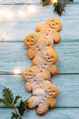 gingerbread cookies or gingerman arranged on a blue wooden table with holly, traditional Christmas plant, and Christmas lights - 396663380