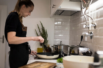 Young charming Swedish woman cooking at home in her kitchen, preparing healthy mediterranean food for her family. Young food blogger doing food preparation in her kitchen, frying vegetables