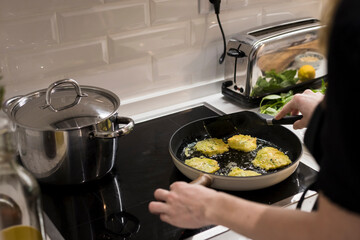 Young charming Swedish woman cooking at home in her kitchen, preparing healthy mediterranean food for her family. Young food blogger doing food preparation in her kitchen, frying vegetables