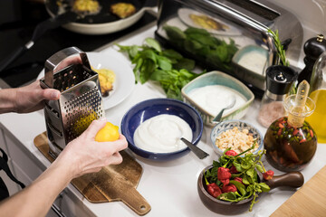 Close up of woman's hands garnishing fresh healthy food with fresh lemon and yogurt. Young food blogger preparing vegetarian food for her contents. Woman cooking food in the kitchen
