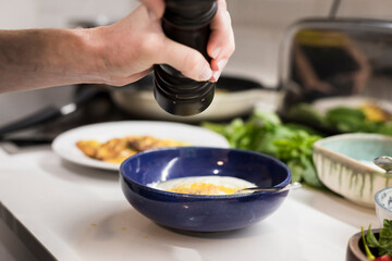 Close up of Woman's hand garnishing fresh vegetarian food with black pepper. Young food blogger grinding black pepper in a pot for her food preparation while she's cooking in the kitchen 